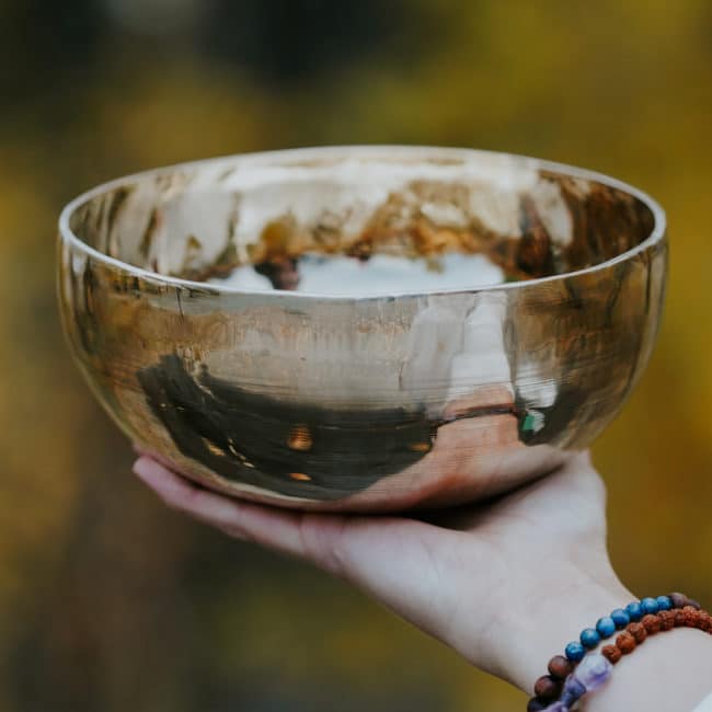 Erin's hand is shown holding her large singing bowl. This is one of the tools she uses as an energy healer at Waters Edge Healing