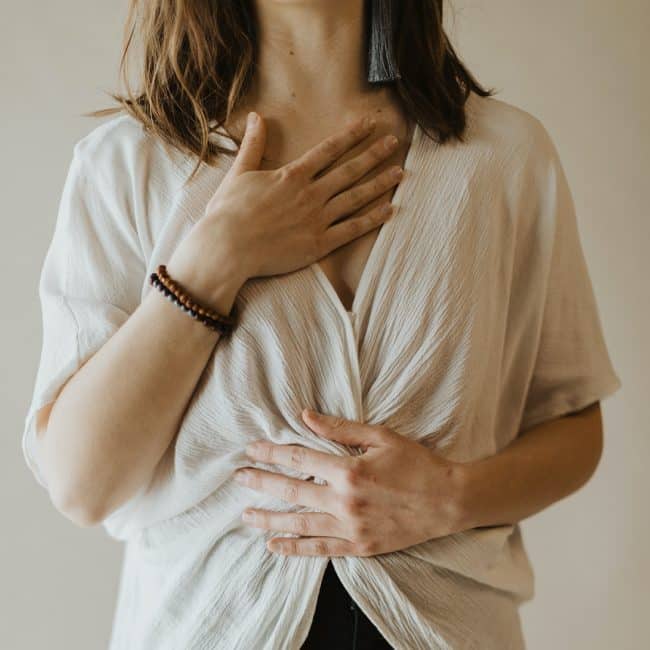 Erin Vivian standing with one hand on her heart and one hand on her belly. This image evokes peace after experiencing Heart-Wall Removal.