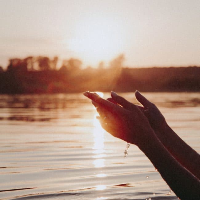 Hands playing in the water at sunset. Releasing water from cupped hands evokes the release of trapped energy using the Body Code.