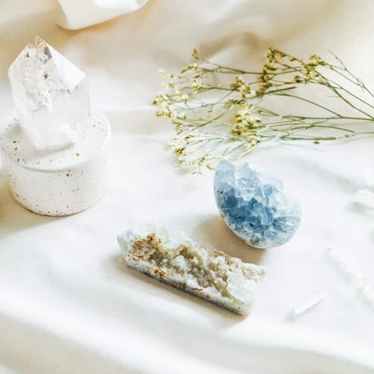 An image of a white cloth covered table with various crystals and plants honoring their energy with a DIY home altar.